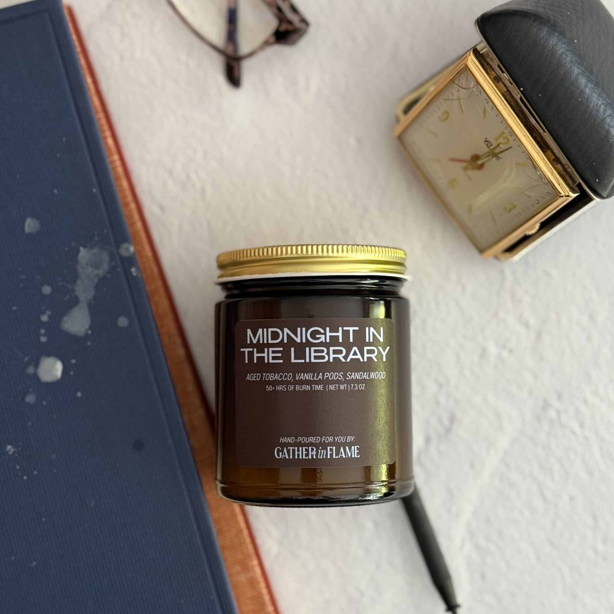 Candle jar labeled 'Midnight in the Library' on a textured surface with a book and clock in the background.