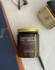 Candle jar labeled 'Midnight in the Library' on a textured surface with a book and clock in the background.
