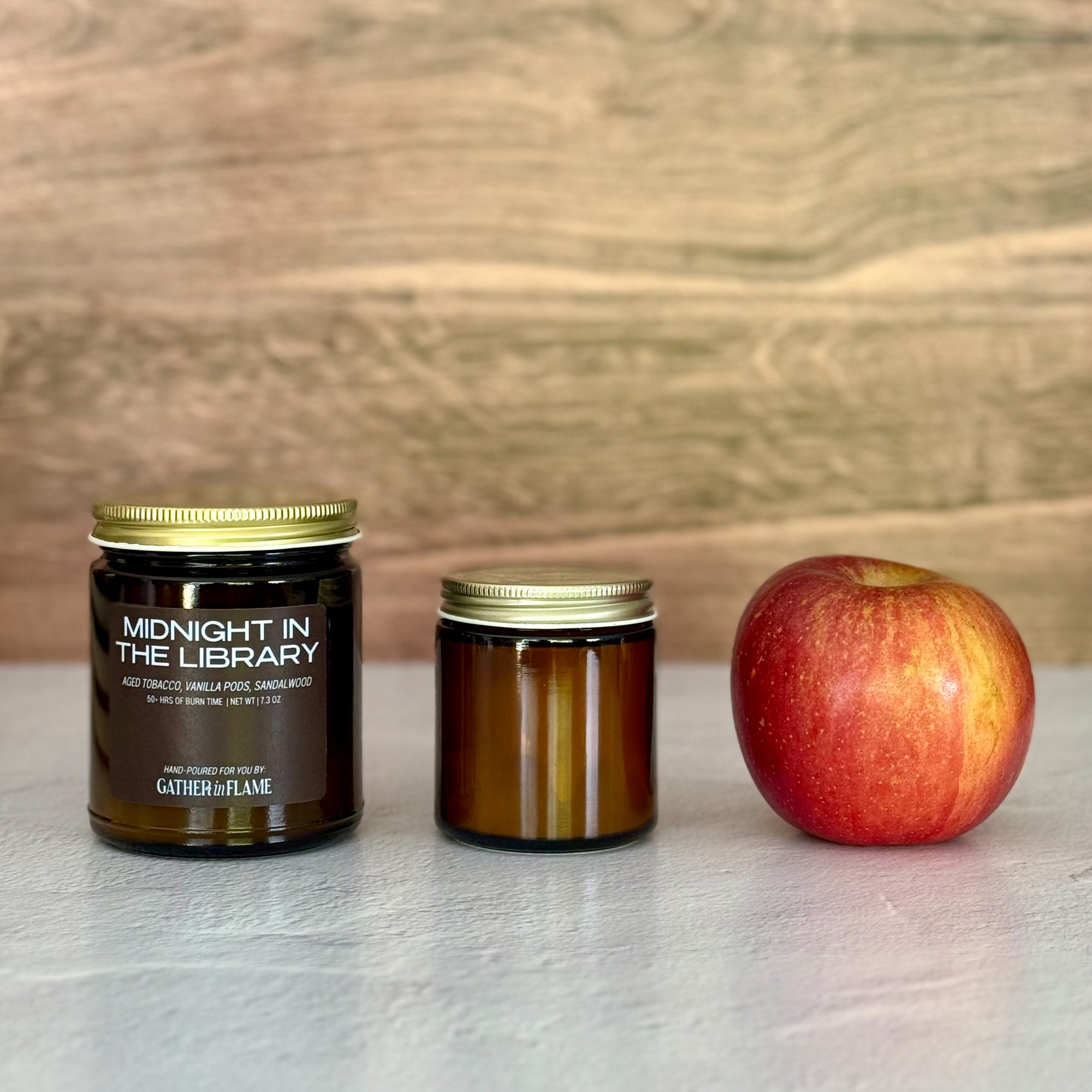 Two candles of different sizes and an apple on a light surface with a wooden background