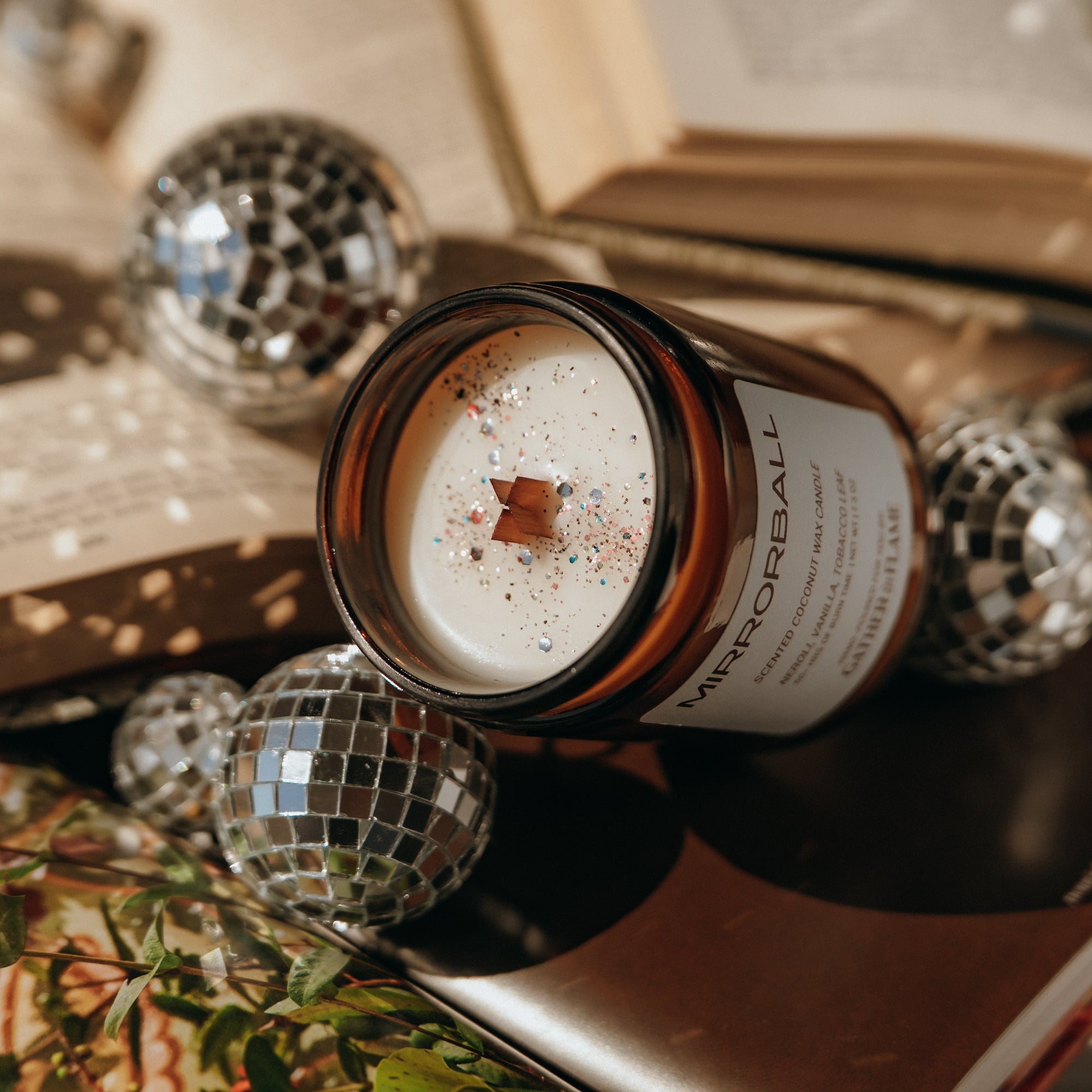 Candle in a glass jar with decorative disco balls and books in the background