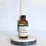 A reed diffuser in a brown bottle labeled 'Oregon Evergreen' and a bundle of reeds inserted into it, presented on a white platform.