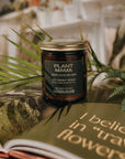 Jar of 'Plant Mama' candle on a book with plants in the background