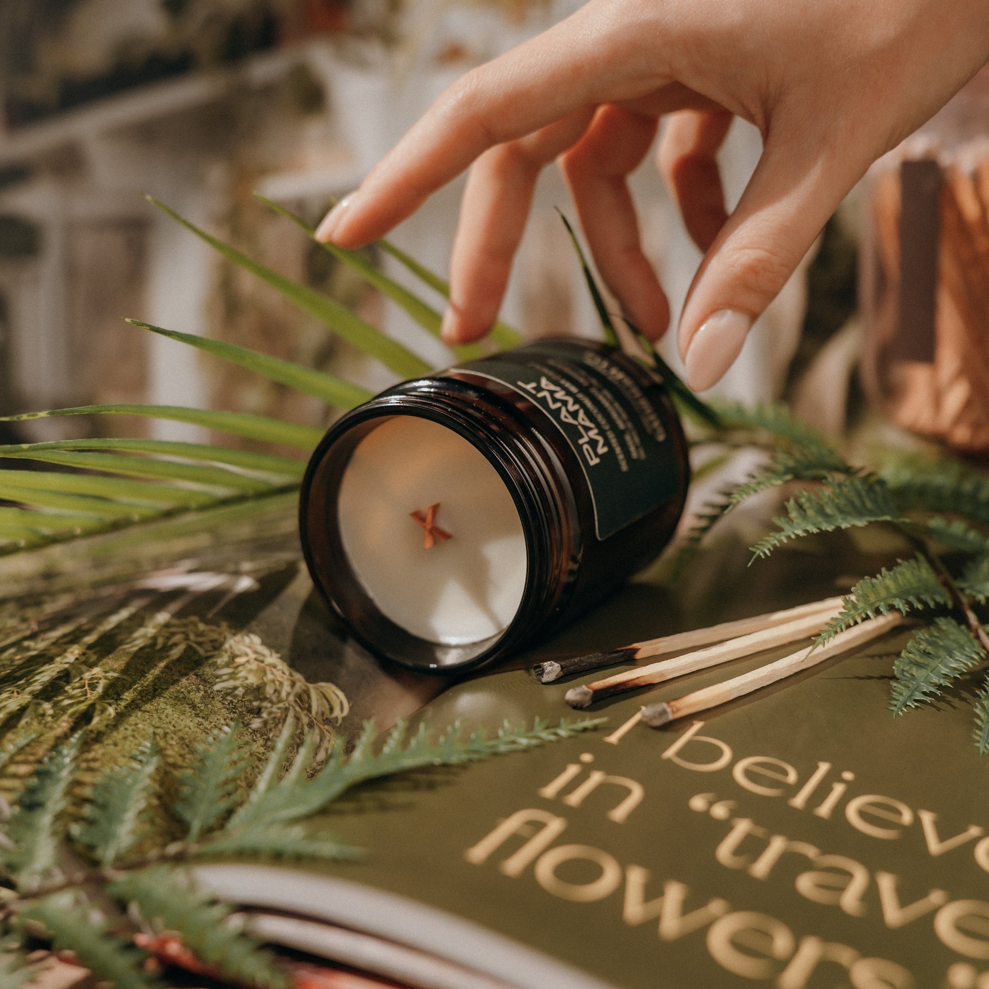 Candle being lit with a hand, surrounded by greenery and a book with text.