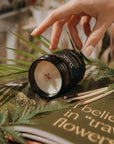 Candle being lit with a hand, surrounded by greenery and a book with text.