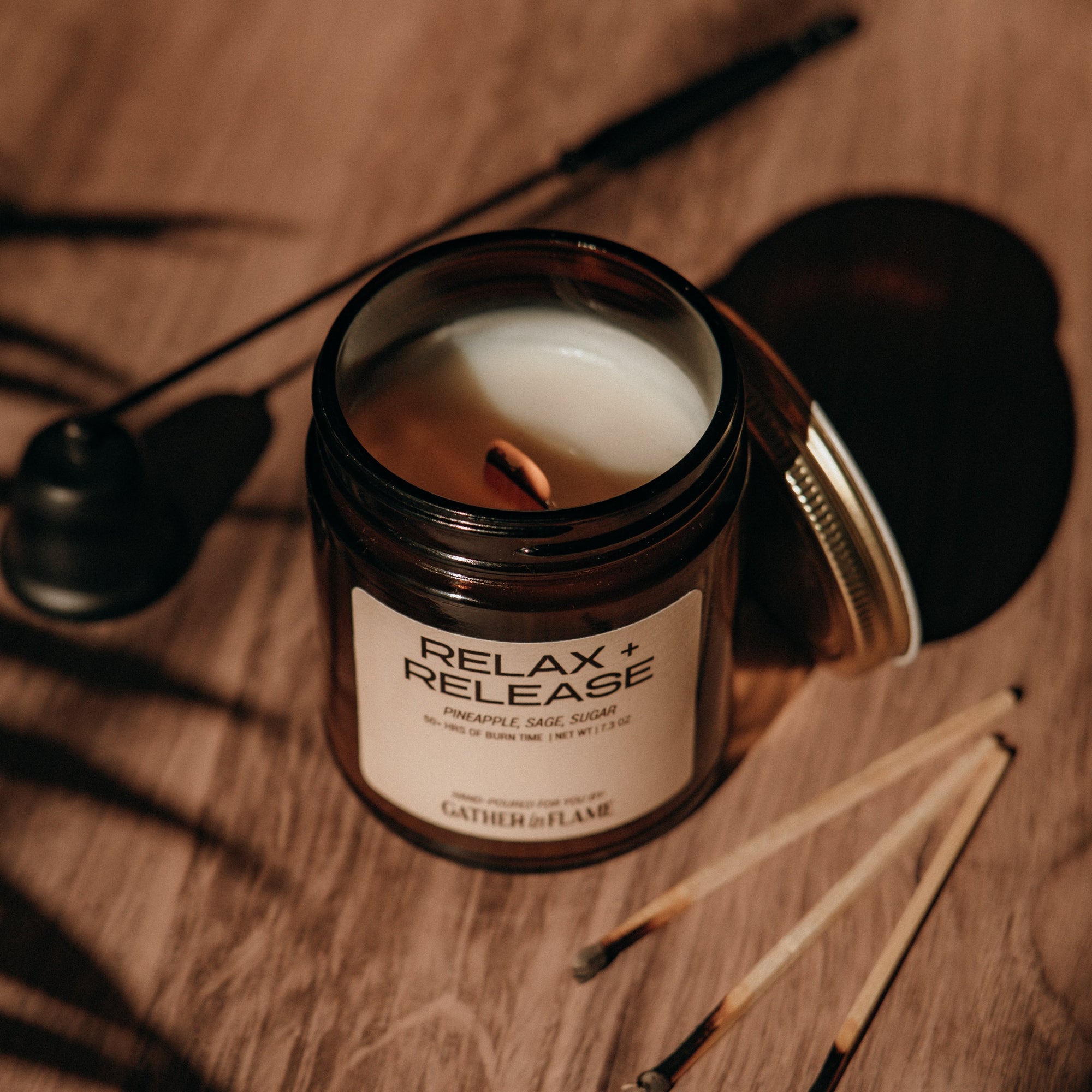 Candle in a jar labeled 'Relax + Release' on a wooden surface with shadows.