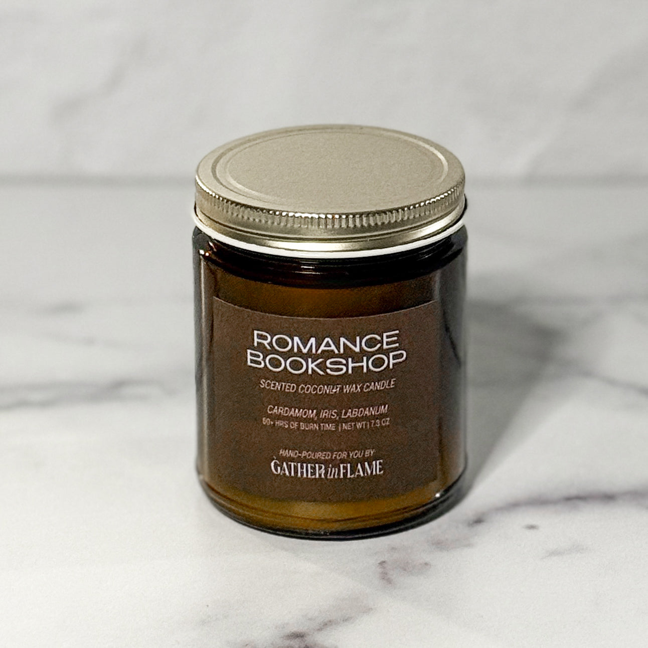 Close up of amber glass jar candle labeled Romance Bookshop with a white background.