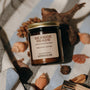 Amber glass candle jar labeled Seaside Reads on a towel surrounded by shells and driftwood.