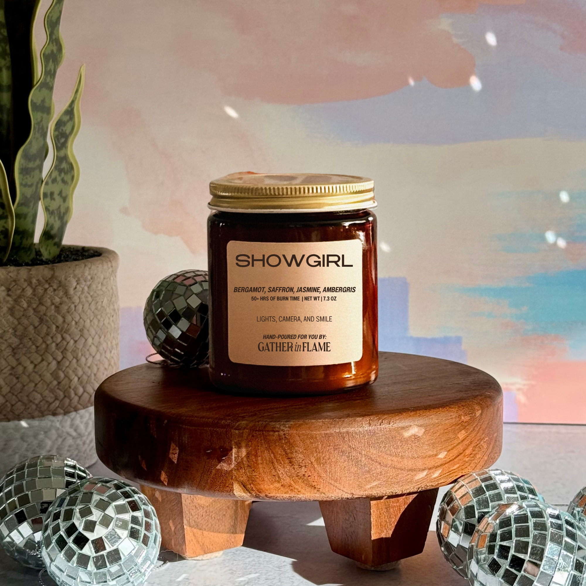 Showgirl swiftie-inspired candle on a wooden stand with disco balls and a plant in the background