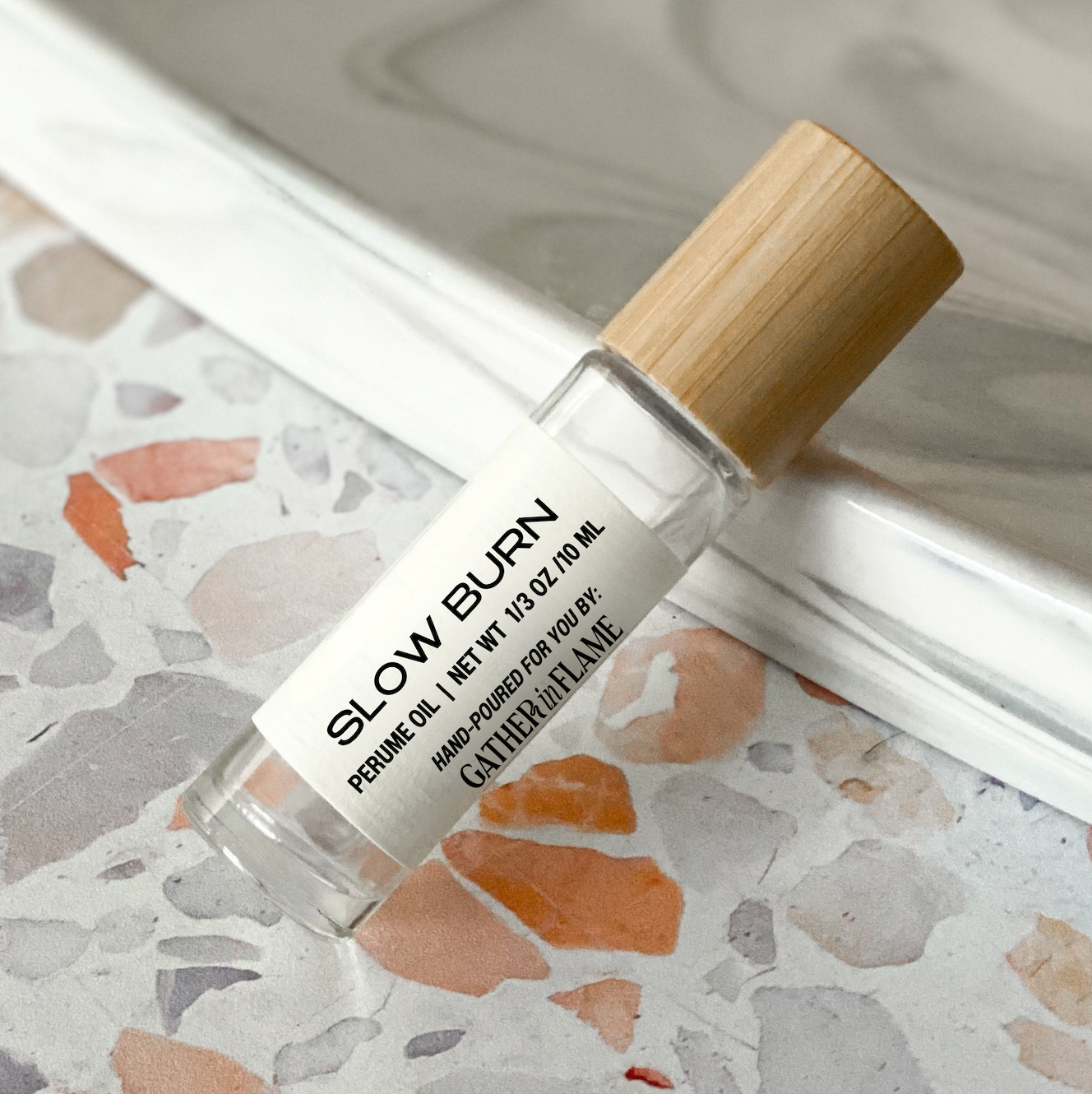 Perfume oil roller labeled 'Slow Burn' on a terrazzo surface
