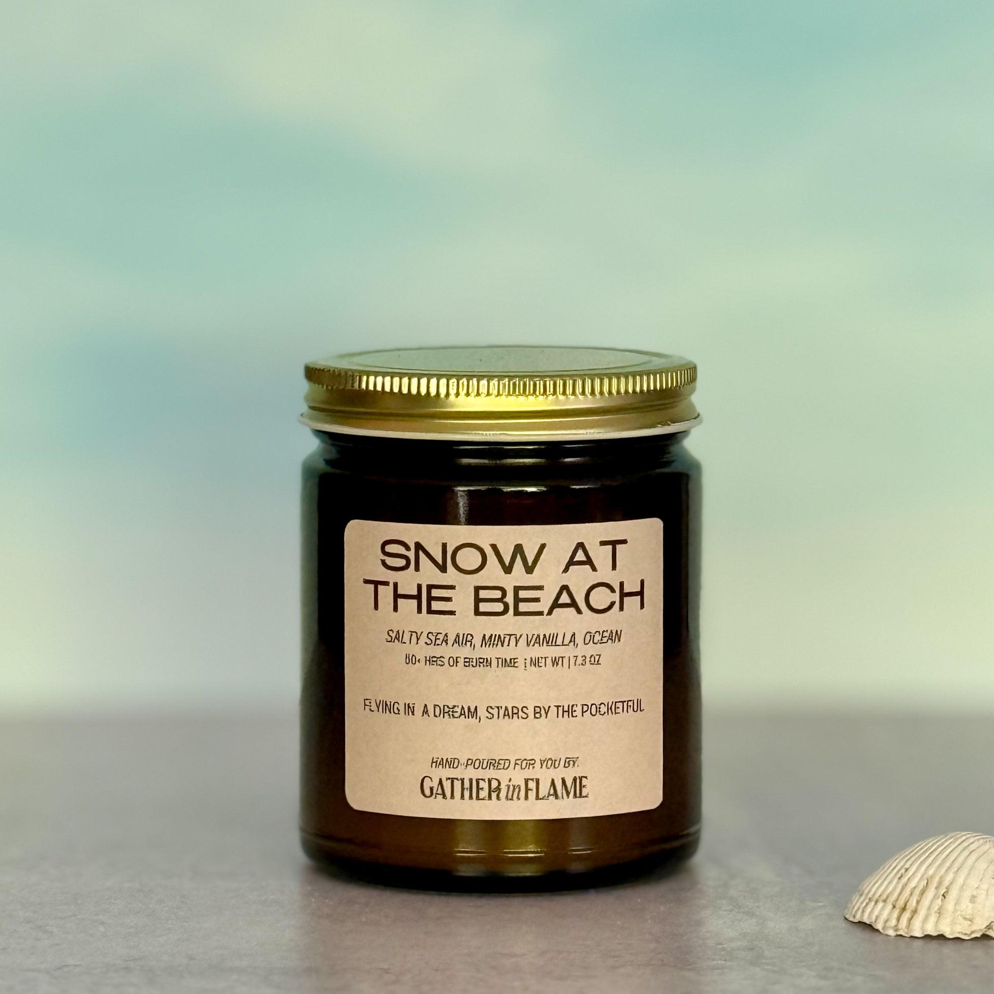 Candle jar labeled 'Snow at the Beach' with a gold lid on a blurred background