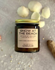 Flatlay showing candle labeled 'Snow at the Beach' by Gather 'n Flame on a textured surface with decorative elements.