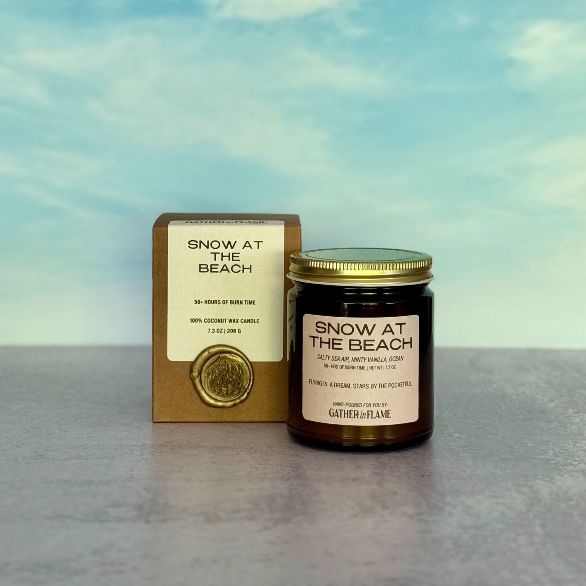 Candle labeled 'Snow at the Beach' with packaging against a blue sky background