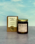 Candle labeled 'Snow at the Beach' with packaging against a blue sky background