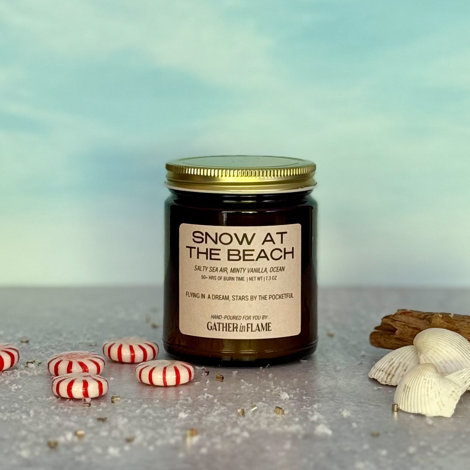 Candle jar labeled 'Snow at the Beach' with decorative items on a neutral background