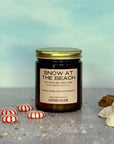 Candle jar labeled 'Snow at the Beach' with decorative items on a neutral background