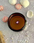 overhead view of lit candle surface with melted wax surrounded by peppermint candies and cinnamon sticks on a gray surface