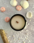 overhead view of candle surface with wood wick surrounded by peppermint candies and cinnamon sticks on a gray surface