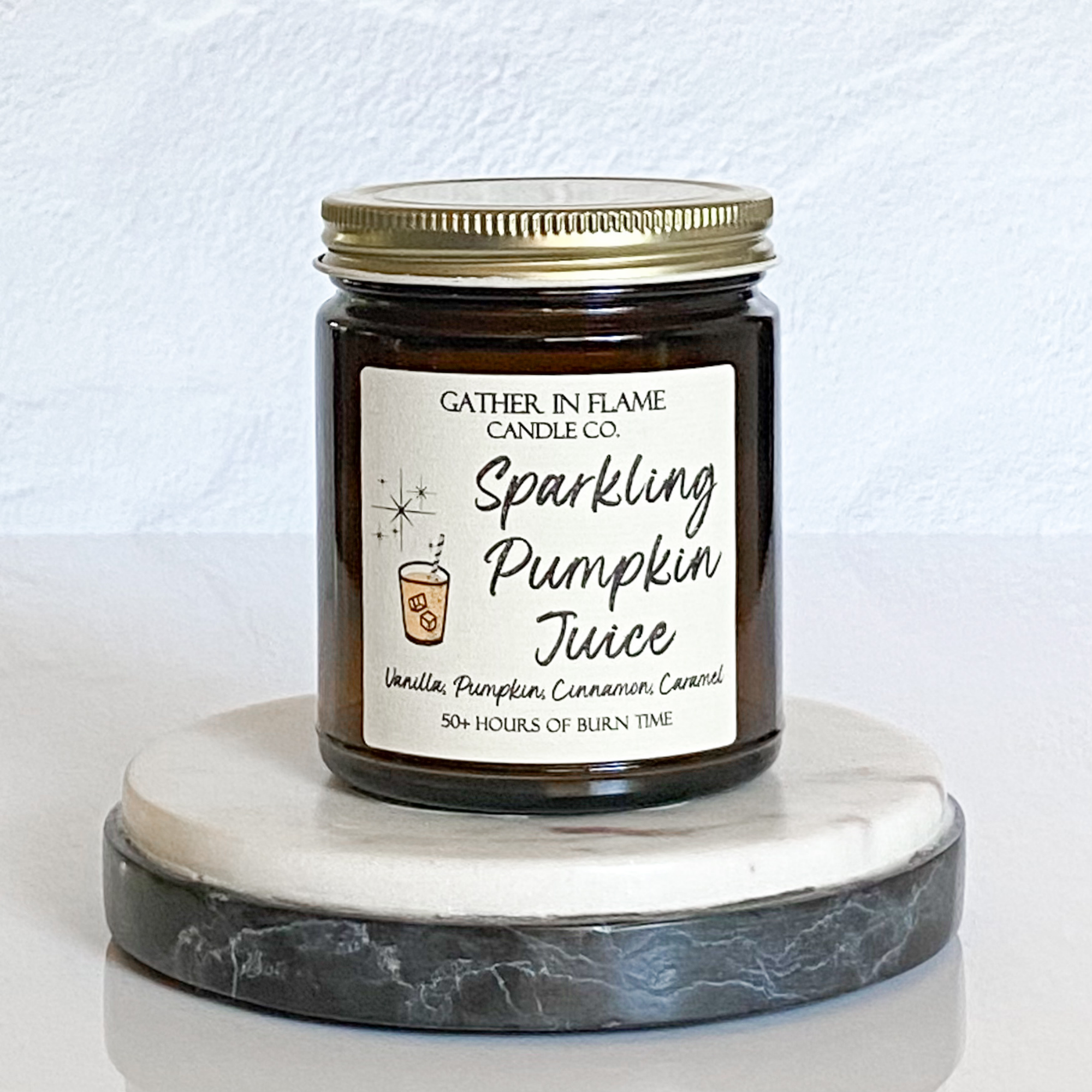 A jar candle with a label reading 'Sparkling Pumpkin Juice' on a marble-like surface.
