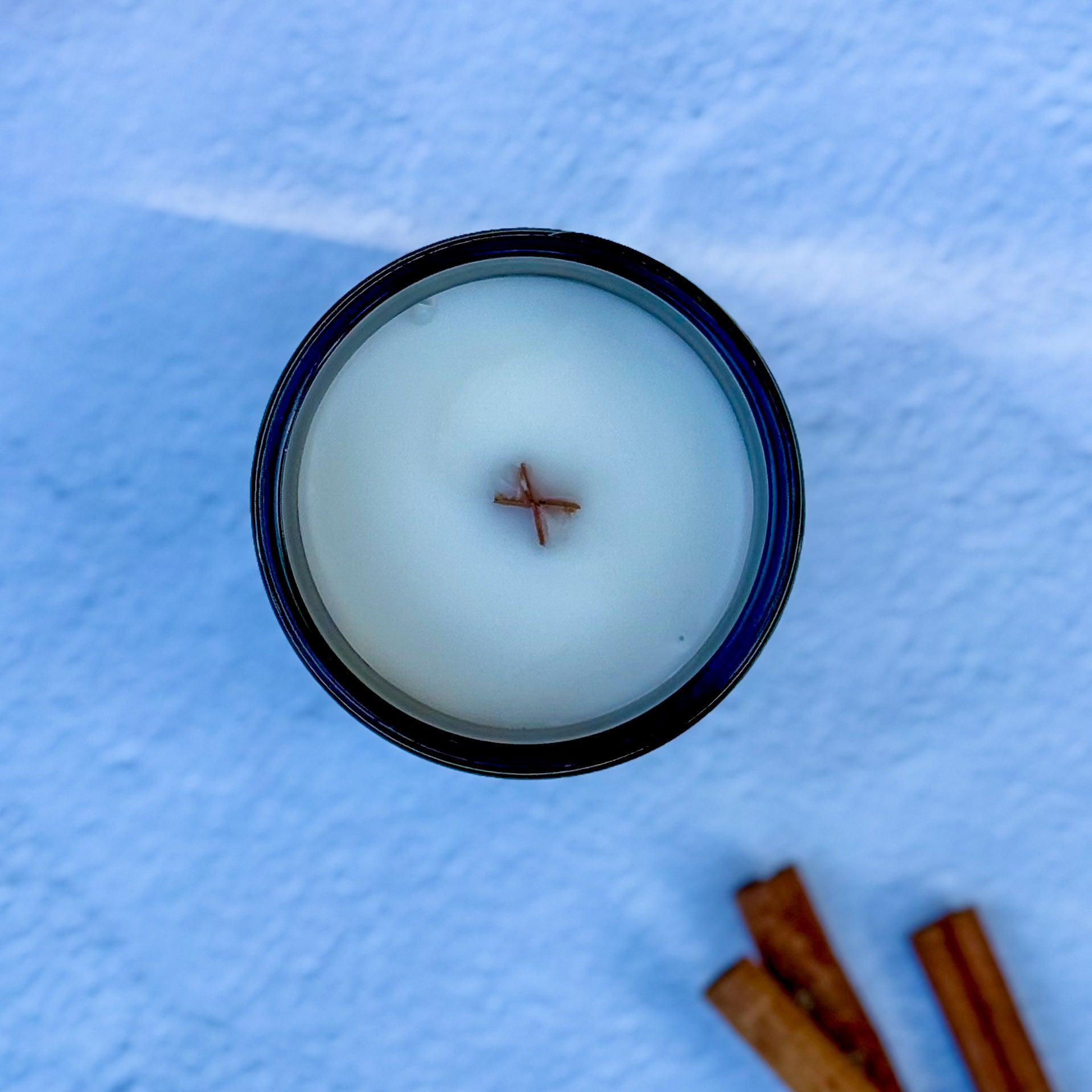Overhead photo of a candle surface with wood wick and cinnamon sticks on light background