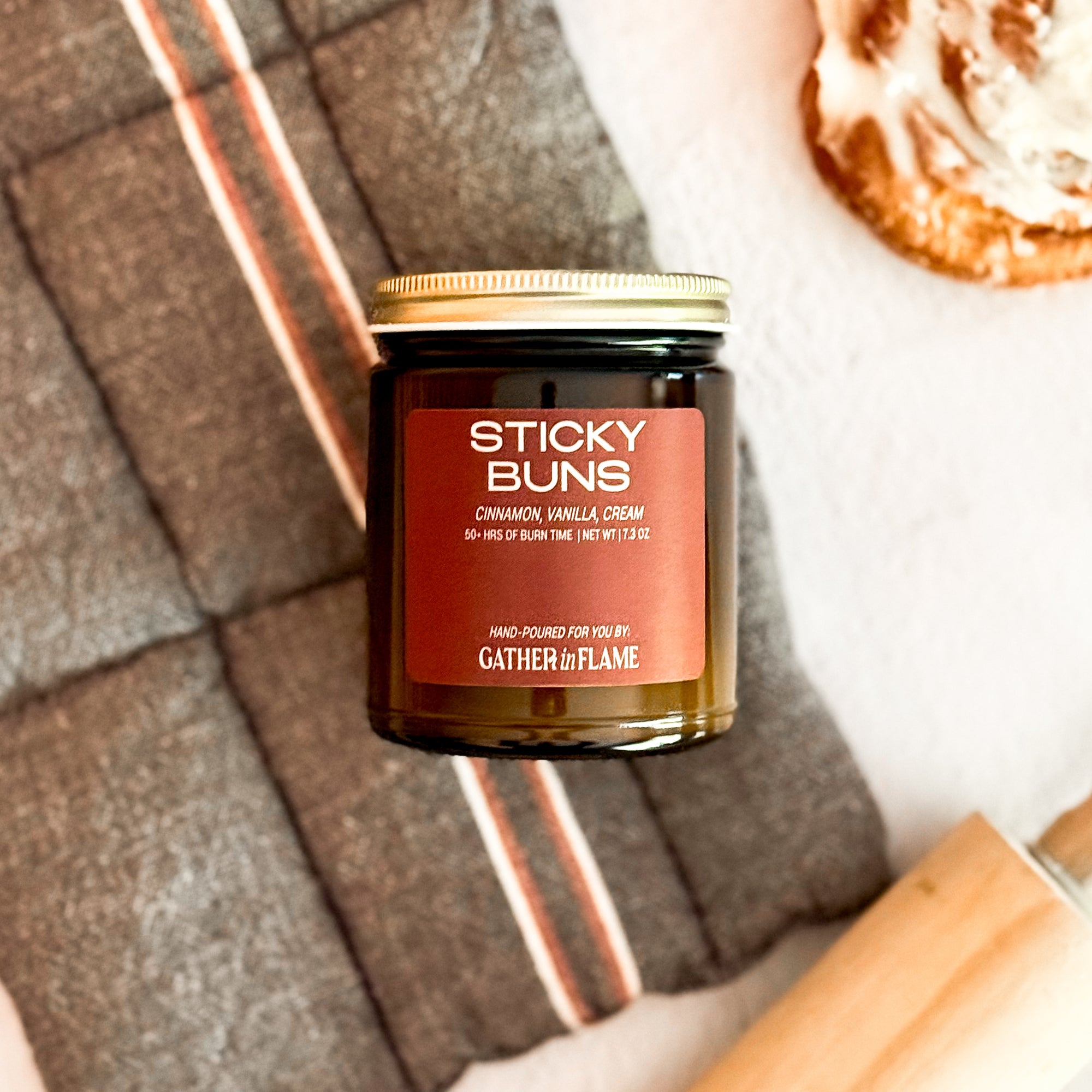 Candle labeled 'Sticky Buns' with a cinnamon roll and rolling pin on a light surface