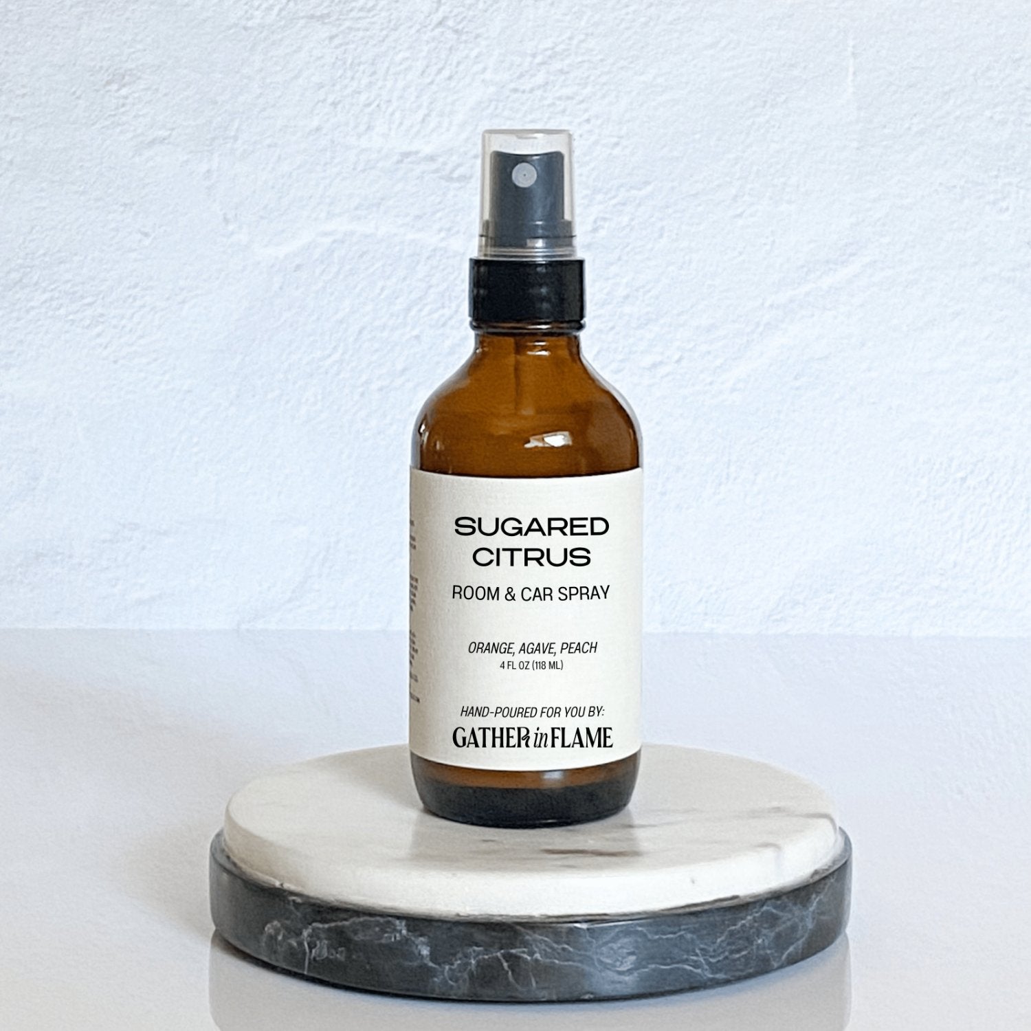 A brown amber spray bottle labeled 'Sugared Citrus' by Gather In Flame Candle Co. on a white marble surface.