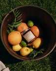 Sugared Citrus candle jar surrounded by fruits in a wooden barrel on grass