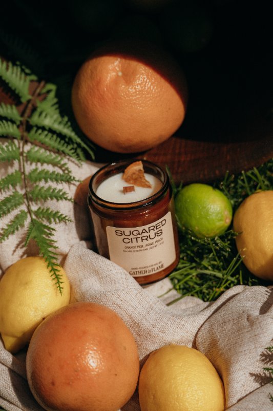 Sugared Citrus candle surrounded by fruits and leaves on a textured surface