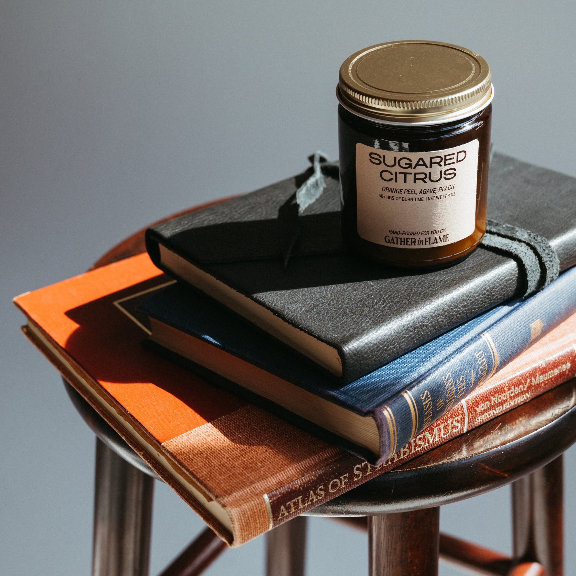 Jar of 'Sugared Citrus' candle on a stack of books with a gray background