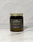 Amber glass candle Labeled The Archives with a white background.