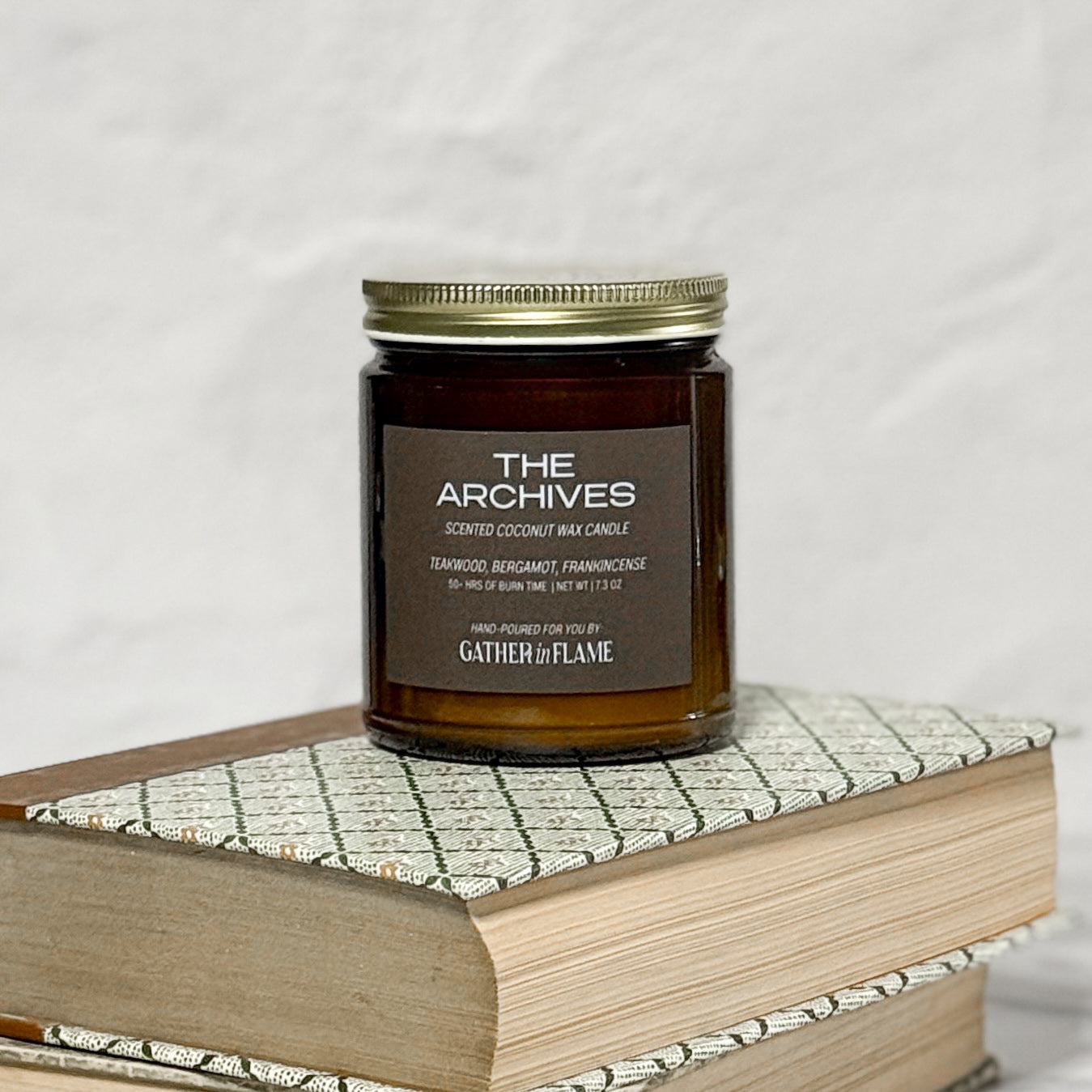 Amber glass candle Labeled The Archives on a stack of books with a white background.