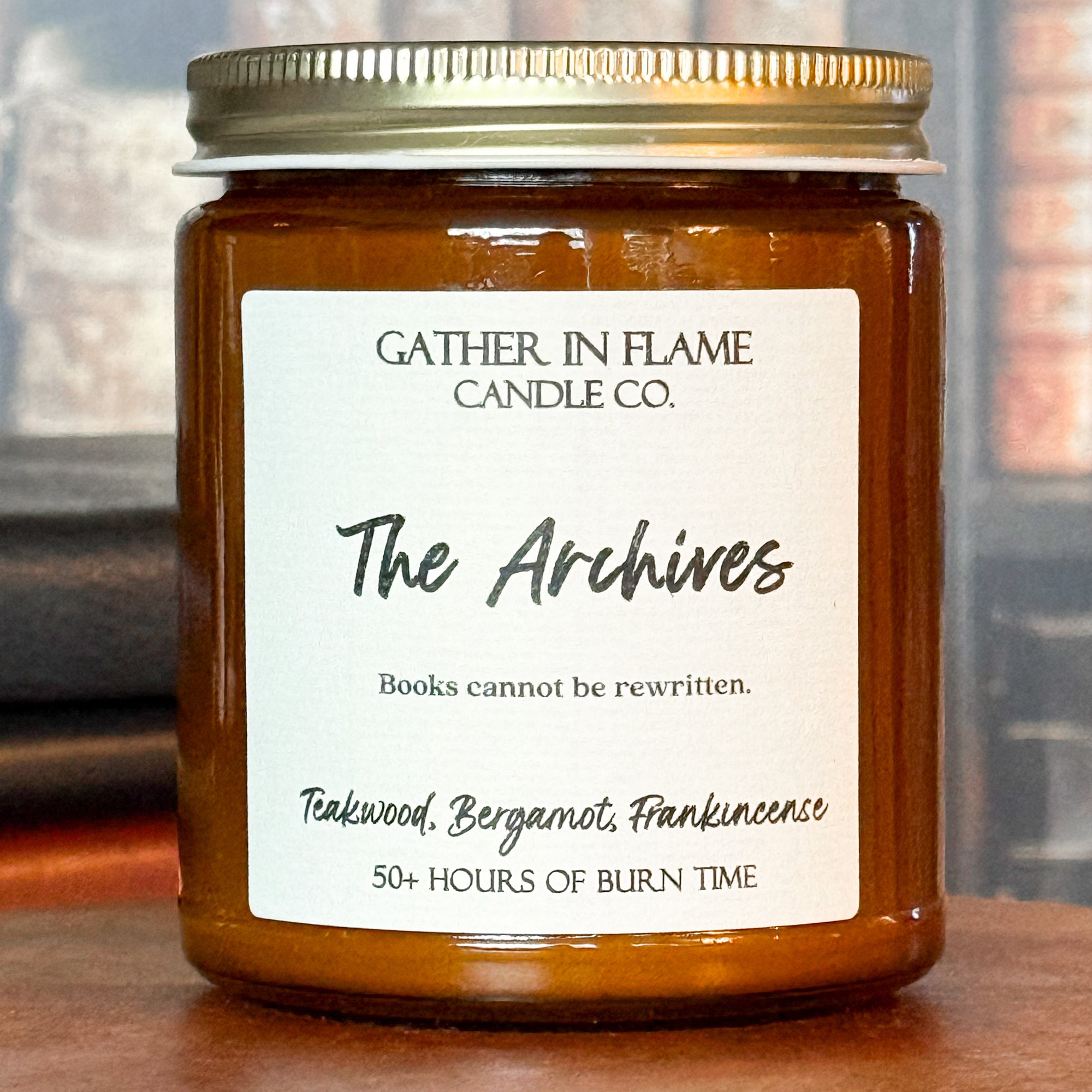 Close up of a jar candle labeled 'The Archives' with a wooden base, set against a backdrop of books.