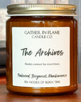 Close up of a jar candle labeled 'The Archives' with a wooden base, set against a backdrop of books.