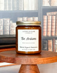 A jar candle labeled 'The Archives' with a wooden base, set against a backdrop of books.