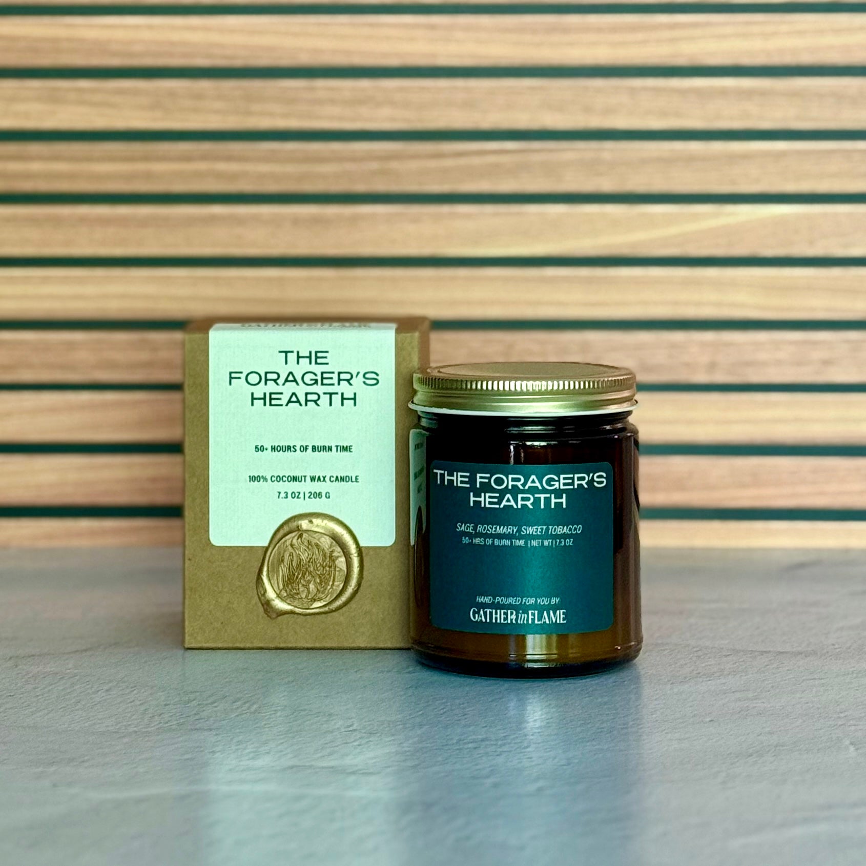 Candle labeled The Forager's Hearth with packaging on wooden background