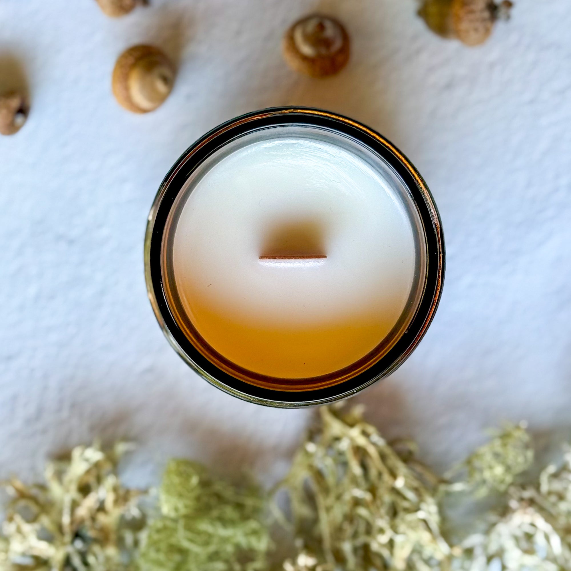 Overhead view of candle with wood wick surrounded by acorns and moss