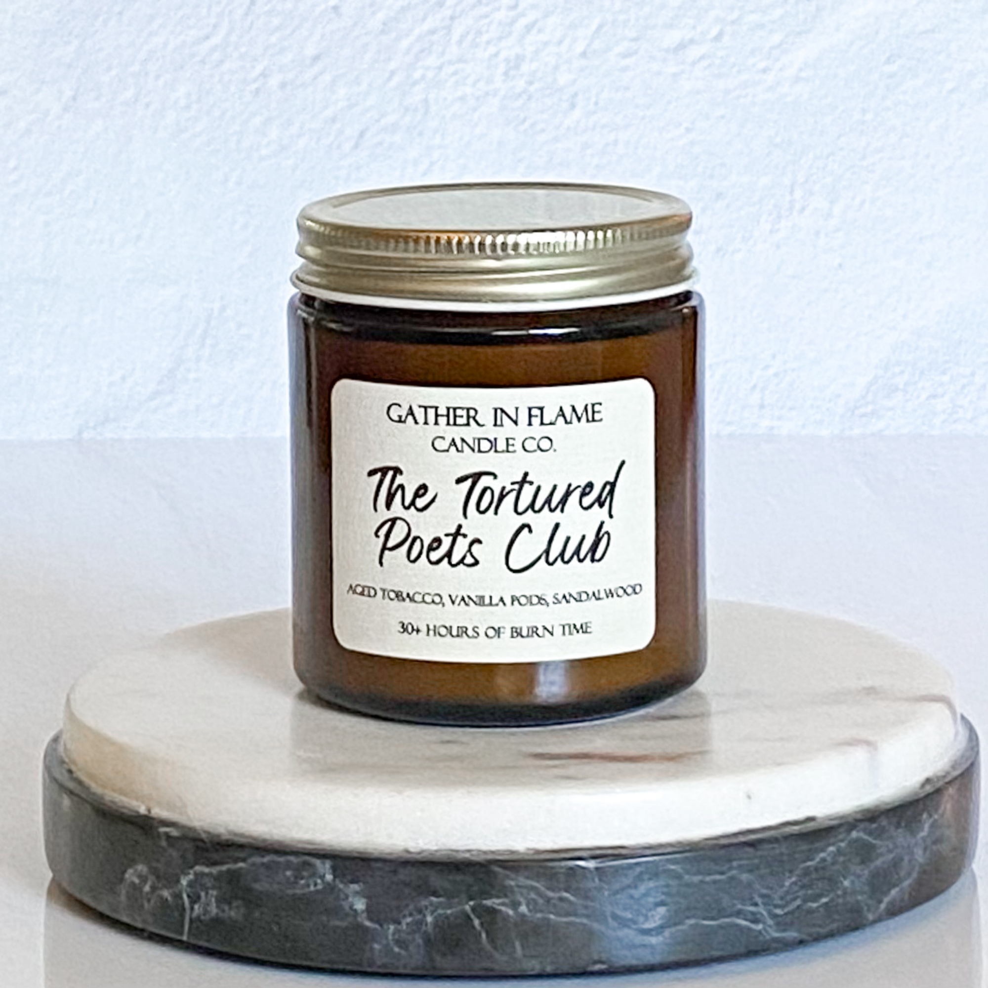 A jar candle with a label reading 'The Tortured Poets Club', with a white and gray marble coaster in the background.