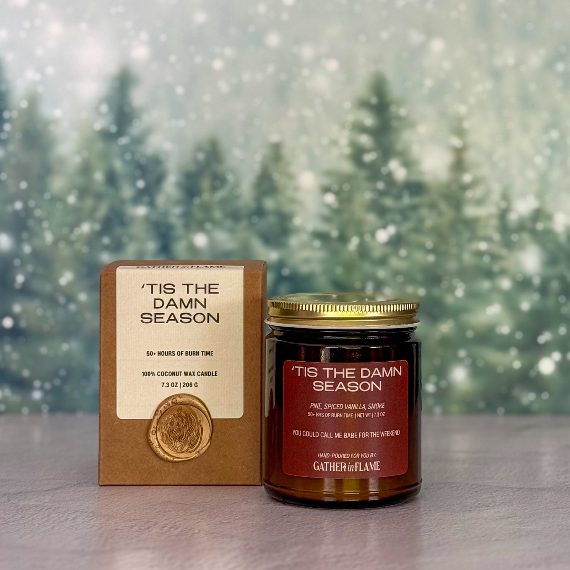 Candle and packaging with 'Tis the Damn Season text against a snowy background