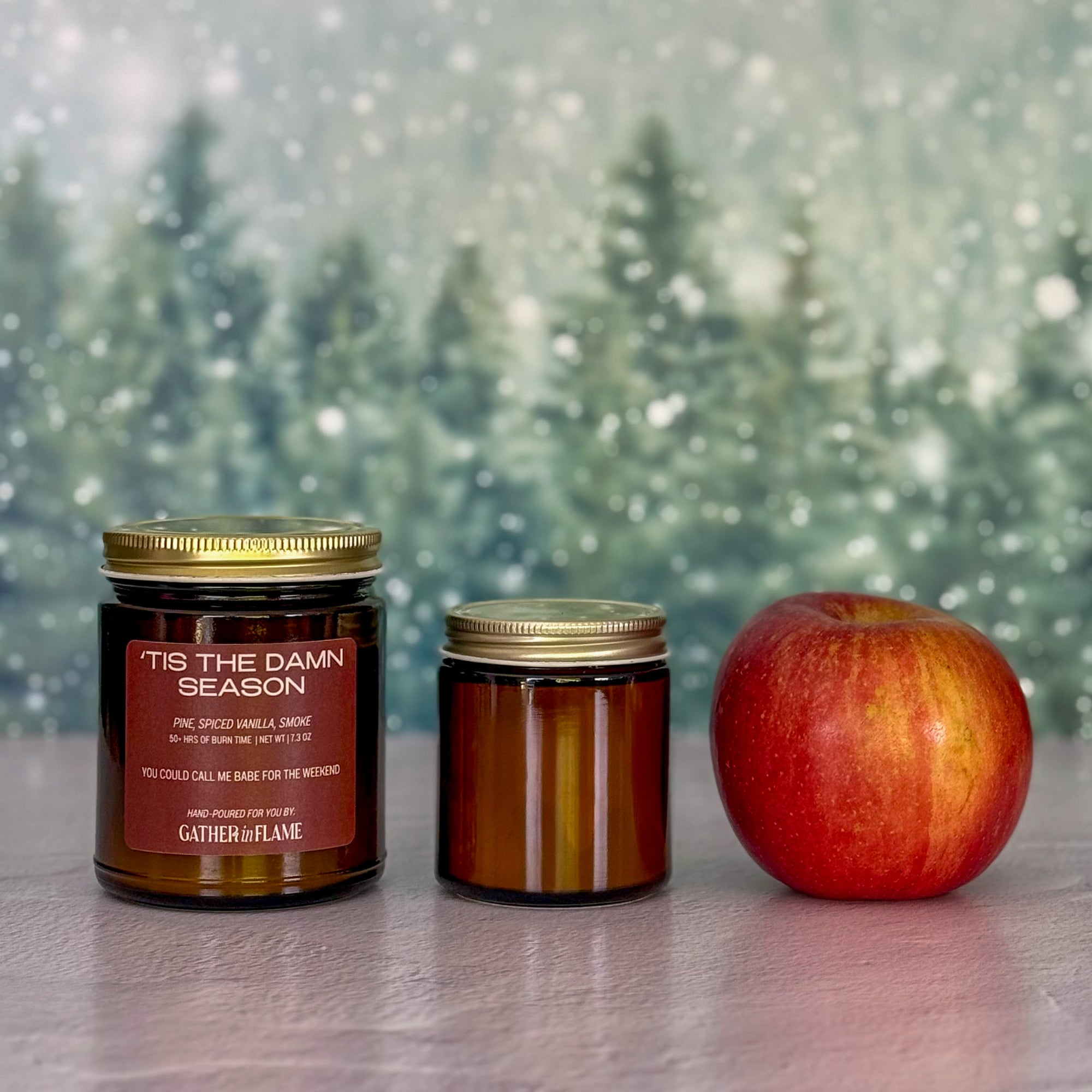Two candles of different sizes and an apple on a surface with a snowy background
