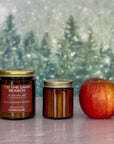 Two candles of different sizes and an apple on a surface with a snowy background