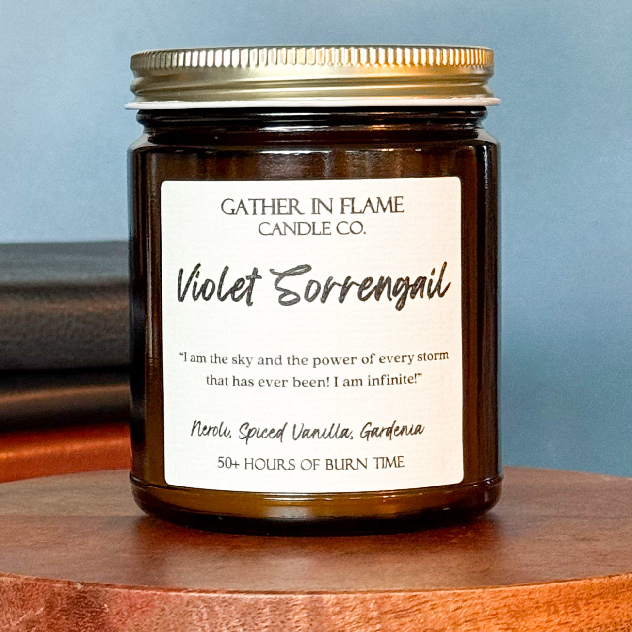 Close up of a jar candle with a label reading 'Violet Sorrengail', placed on a wooden stand, with books in the background.