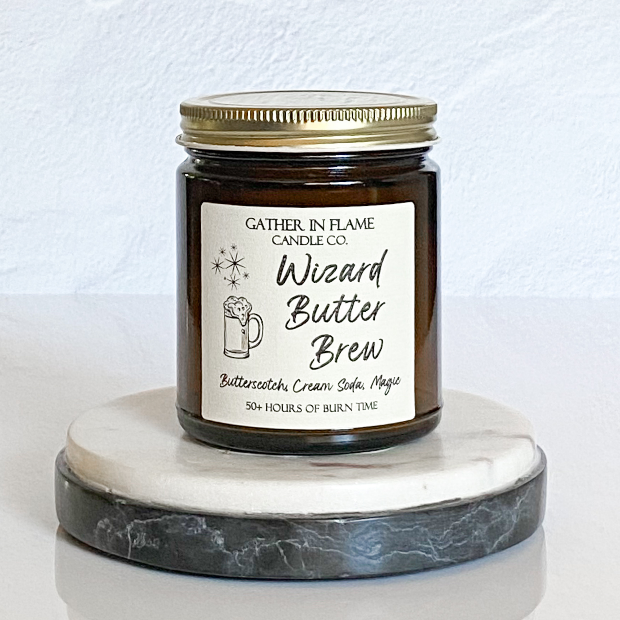 A jar candle with a cream label that reads 'Wizard Butter Brew' with a illustration of a mug, on a marble surface.