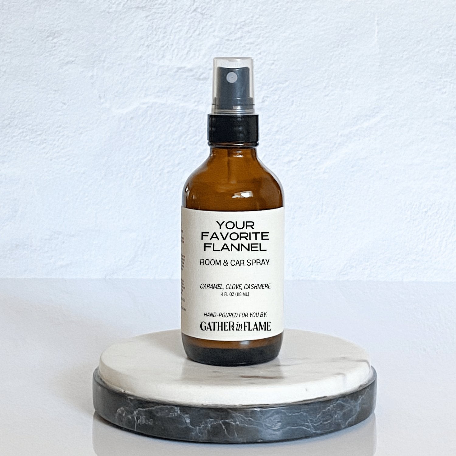 A brown amber spray bottle labeled 'Your Favorite Flannel' by Gather In Flame Candle Co. on a white marble surface.