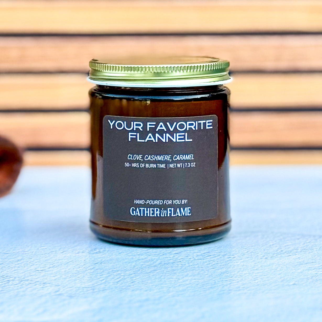 Candle jar labeled 'Your Favorite Flannel' by Gather in Flame on a wooden surface.