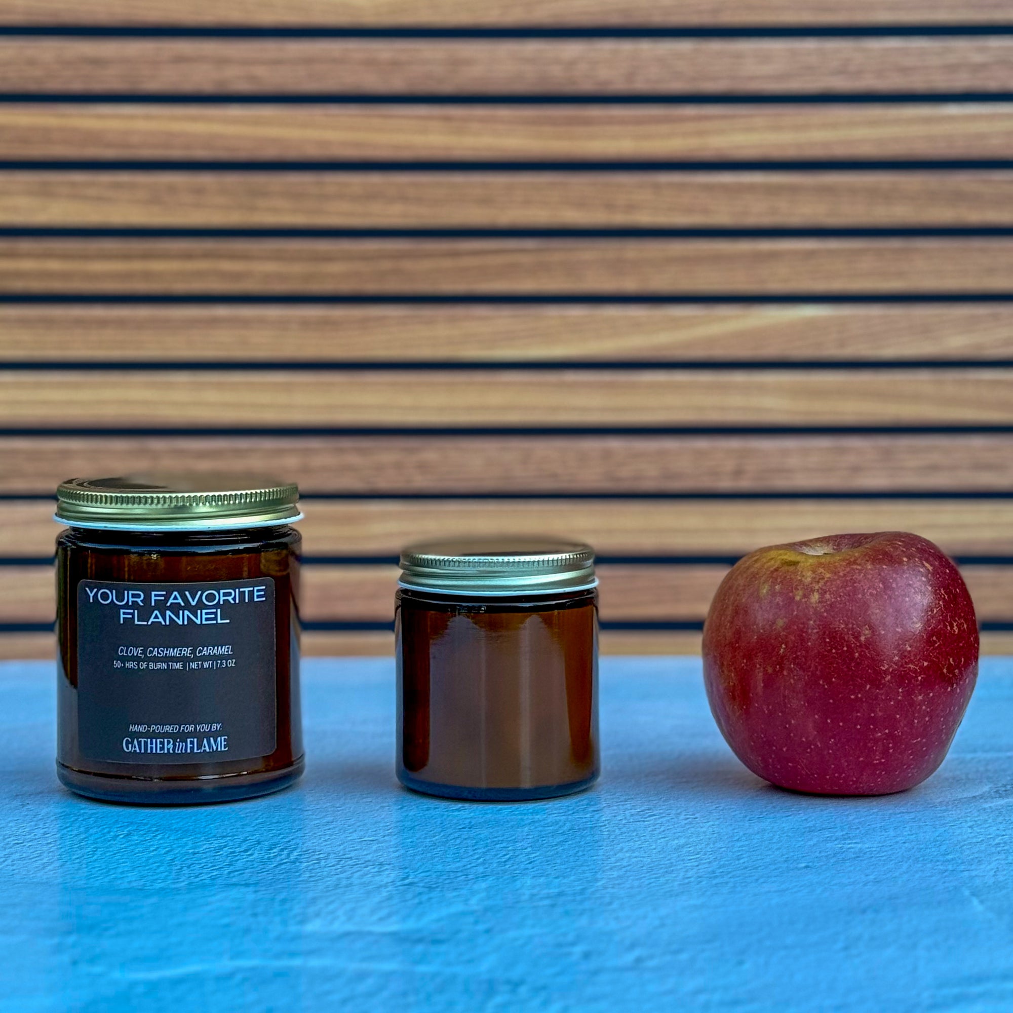 Two candles of different sizes and an apple on a blue surface with a wooden background