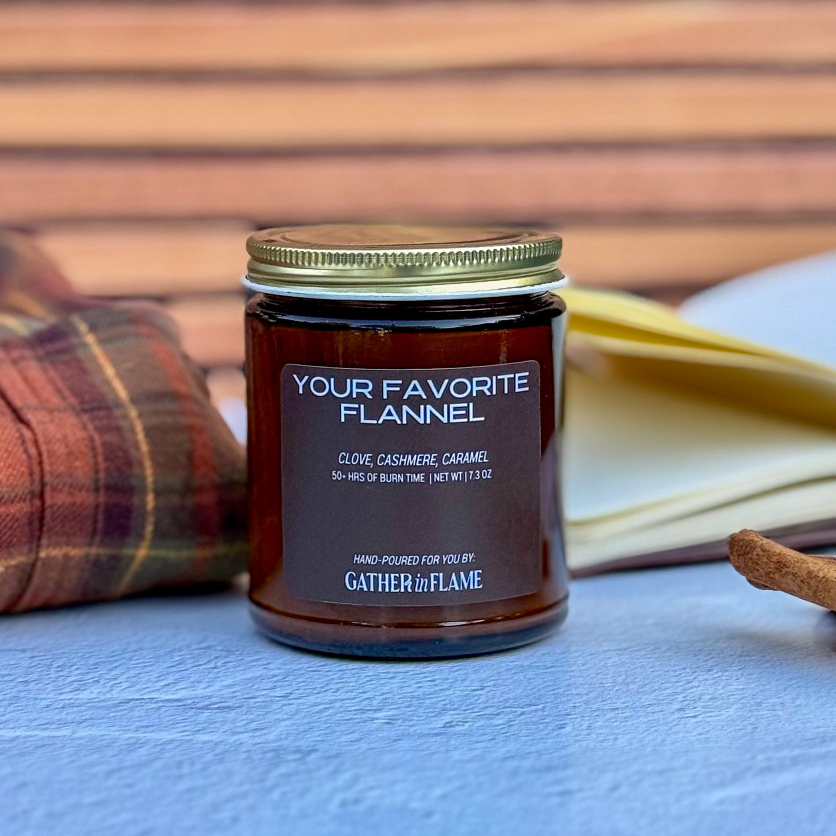 Jar of candle labeled 'Your Favorite Flannel' by Gather the Flame on a wooden surface.