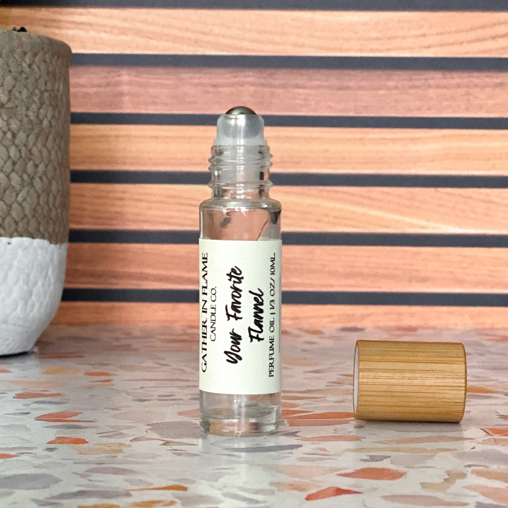 A perfume oil roller with a clear glass body and a bamboo cap sitting beside it, labeled 'Your Favorite Flannel' on a terrazzo surface with wood background.
