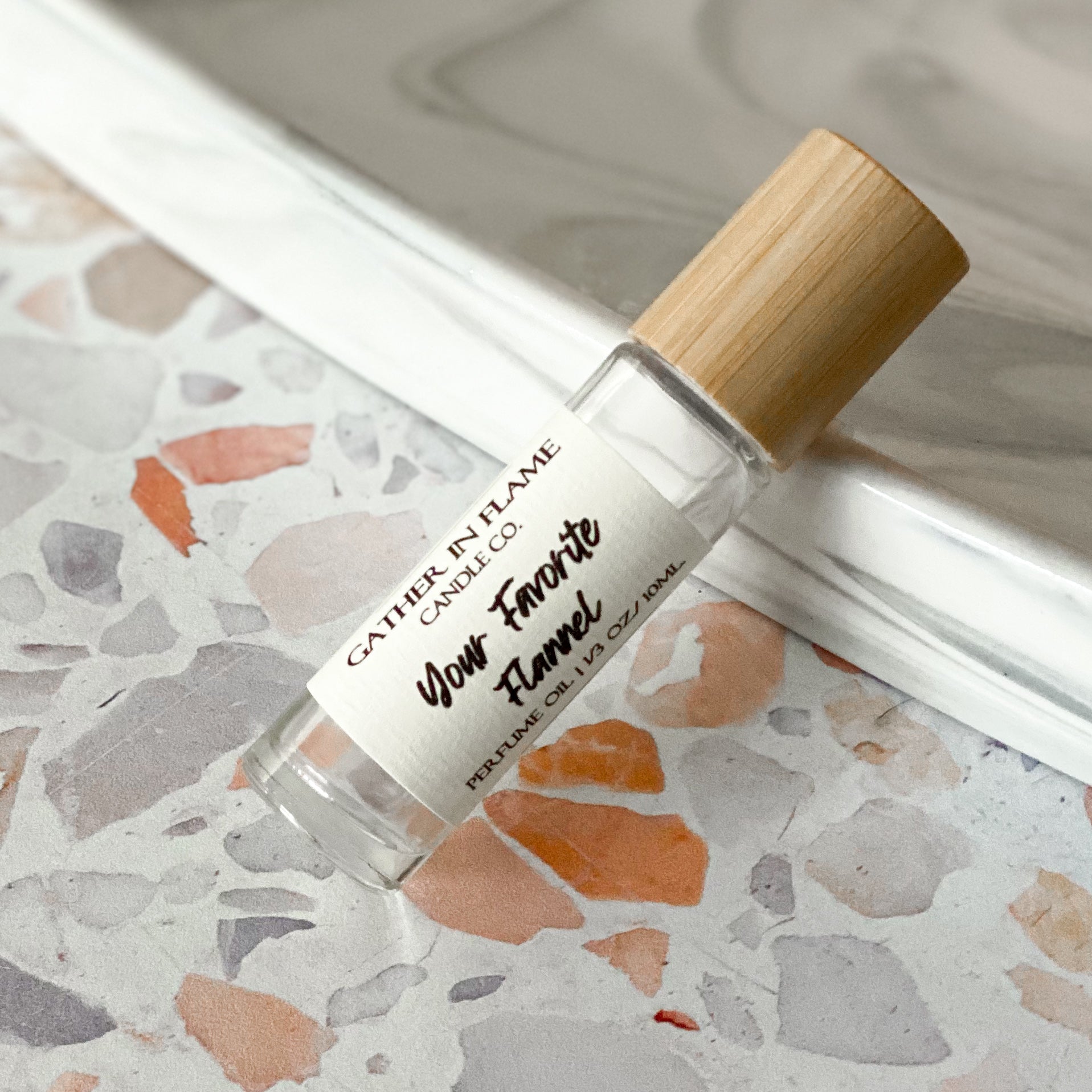 A perfume roller with clear glass bottle and a bamboo wooden cap, labeled with 'Your Favorite Flannel' on a terrazzo surface.