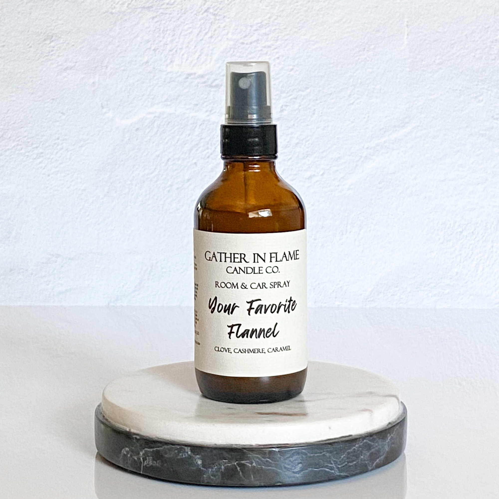 A brown spray bottle labeled 'Your Favorite Flannel' by Gather In Flame Candle Co. placed on a white marble surface.